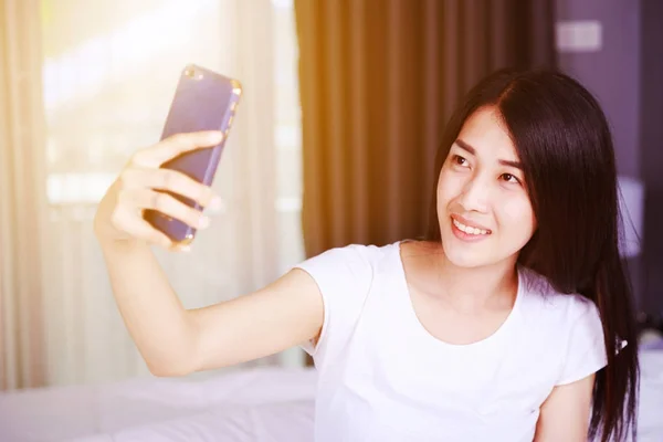 Mujer tomando selfie en cama en dormitorio —  Fotos de Stock