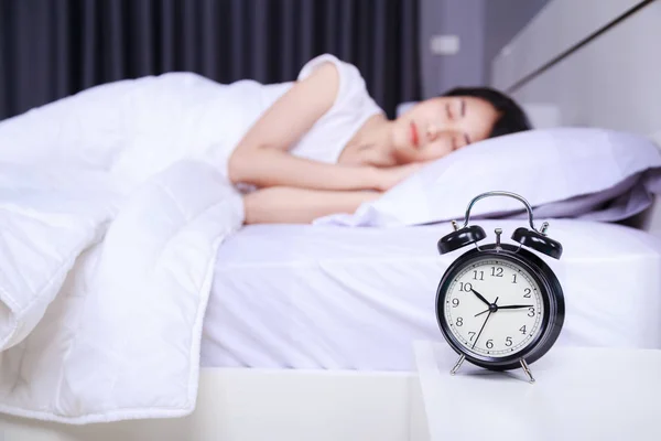 Väckarklocka på bord och kvinnan sover på sängen i sovrummet — Stockfoto