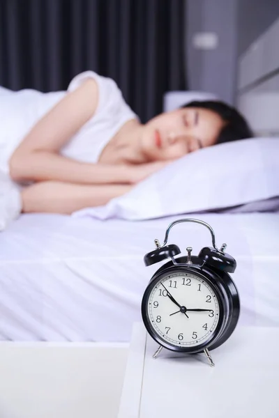 Väckarklocka på bord och kvinnan sover på sängen i sovrummet — Stockfoto