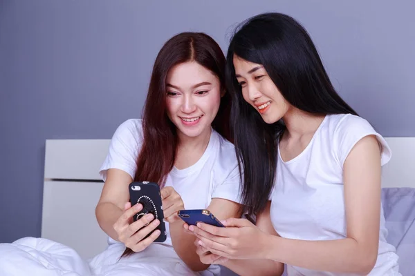 Deux femmes heureuses utilisant un téléphone dans sa main sur le lit dans la chambre — Photo