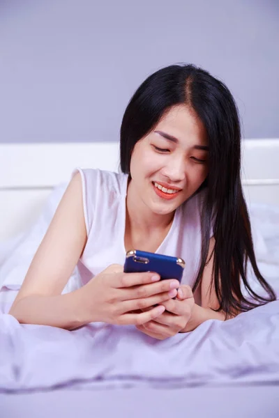 Femme heureuse en utilisant un téléphone dans sa main sur le lit dans la chambre — Photo
