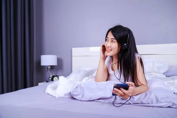 Femme dans les écouteurs écouter de la musique de smartphone sur le lit dans — Photo