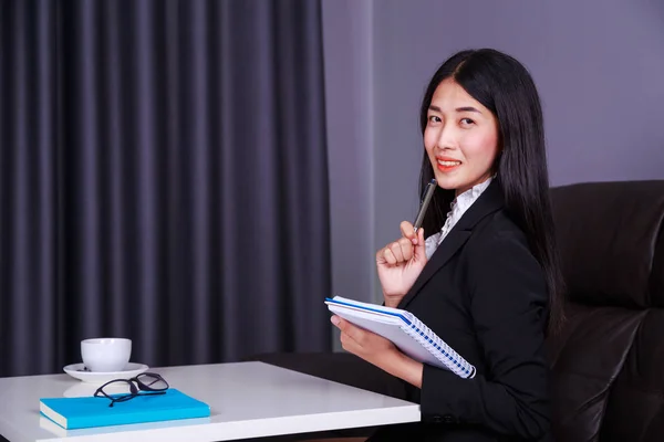 Young business woman sitting at the desk and holding a book — Stock Photo, Image