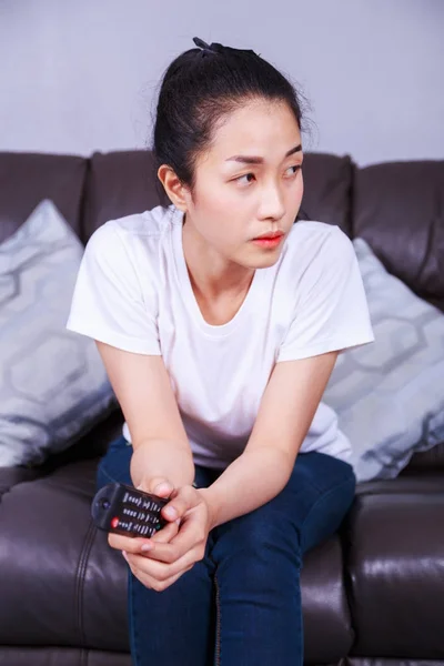 Женщина с пультом дистанционного управления телевизором на диване дома — стоковое фото