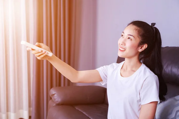 Femme tenant un climatiseur à télécommande sur le canapé à la maison — Photo