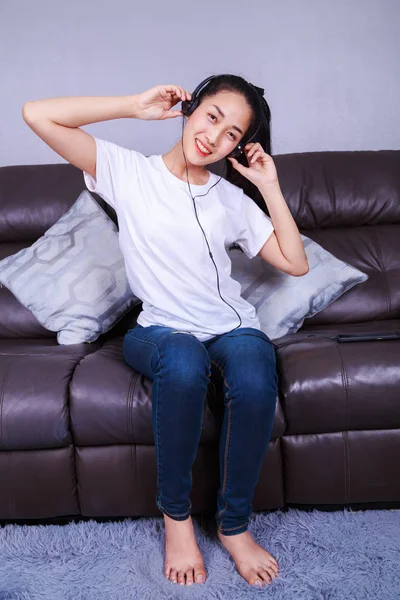 Jovem mulher ouvindo música em fones de ouvido com moblie no sofá — Fotografia de Stock
