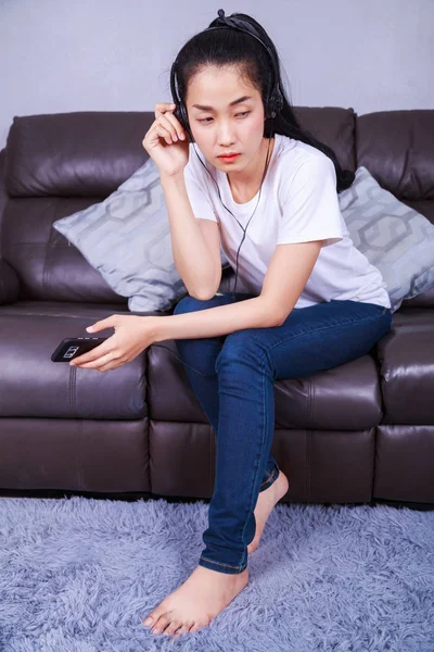 Молодая женщина слушает музыку в наушниках с мобли на диване — стоковое фото