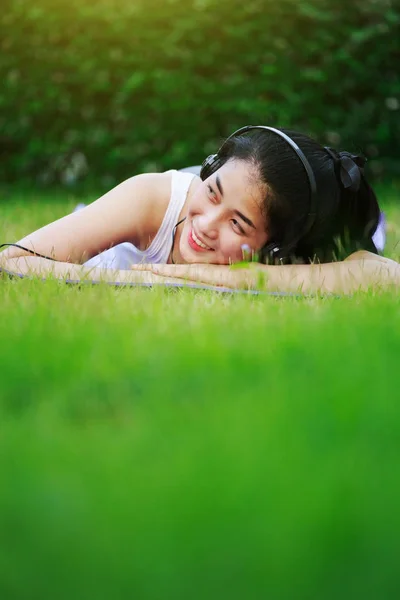 Wanita mendengarkan musik dengan headphone dan berbaring di atas rumput f — Stok Foto