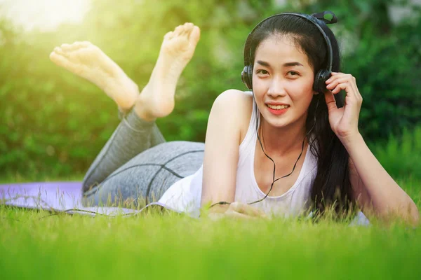 Frau hört Musik mit Kopfhörern und legt sich auf ein Gras — Stockfoto