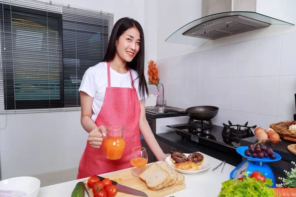 Housewife with pouring orange juice jar in kitchen room — Stock Photo, Image