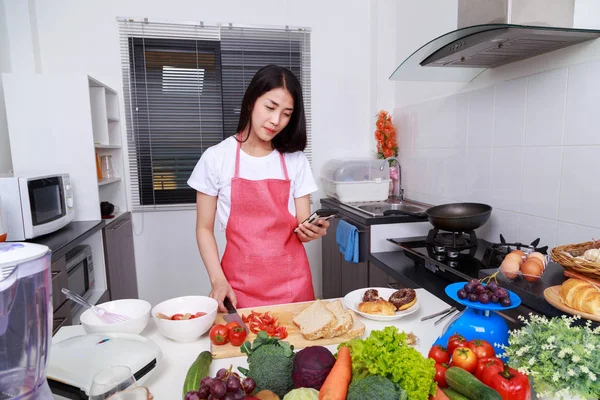 Donna che utilizza il telefono cellulare e cucina in cucina — Foto Stock
