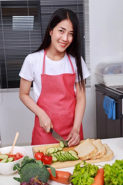 Woman cutting cucumber on board in kitchen room — Stock Photo, Image