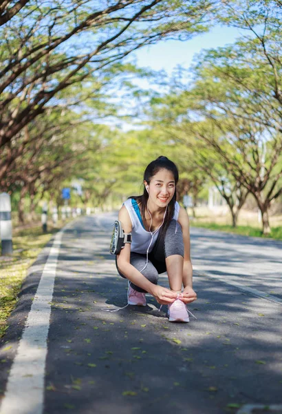 Sporty woman tying shoelaces while listening to music with earph — Stock Photo, Image