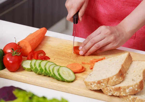 Hand cutting carrot on board in kitchen room — Stock Photo, Image