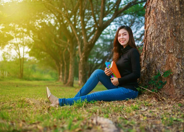 Ung kvinna sitter och håller en bok i parken — Stockfoto