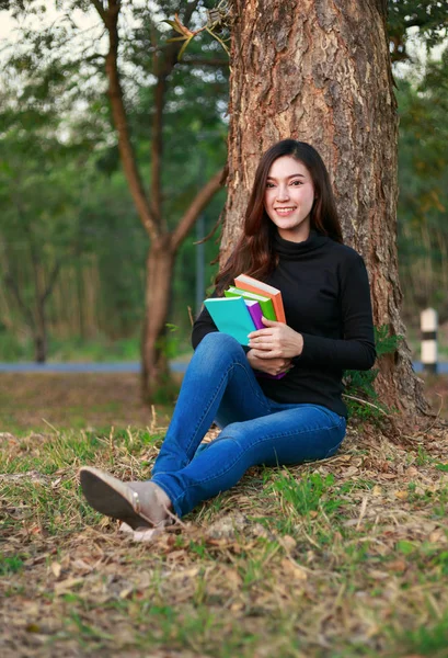 Ung kvinna sitter och håller en bok i parken — Stockfoto