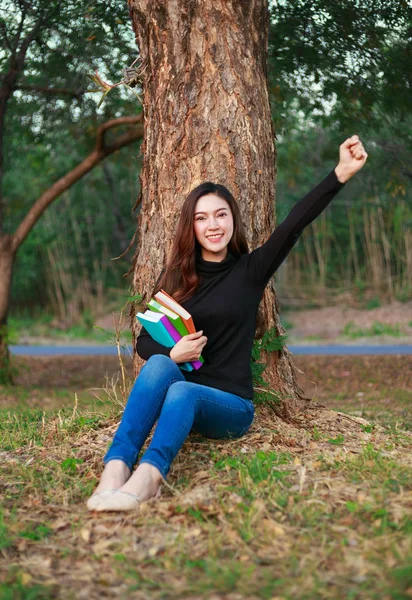 Femme gaie tenant un livre avec le bras levé dans le parc — Photo