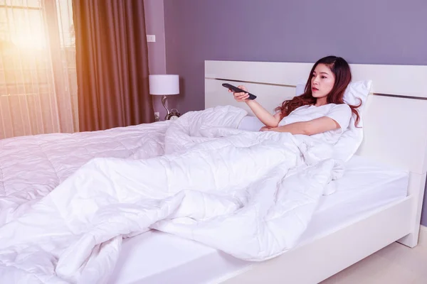 Femme couchée sur un lit avec télécommande et regarder la télévision — Photo