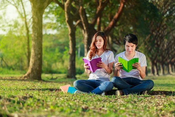 Uomo e donna seduti a leggere un libro nel parco — Foto Stock