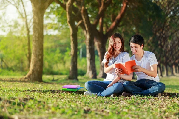 Uomo e donna seduti a leggere un libro nel parco — Foto Stock