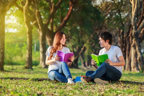 Uomo e donna seduti a leggere un libro nel parco — Foto Stock