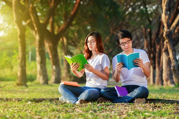 Uomo e donna seduti a leggere un libro nel parco — Foto Stock