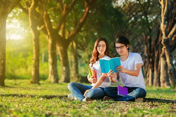 Uomo e donna seduti a leggere un libro nel parco — Foto Stock