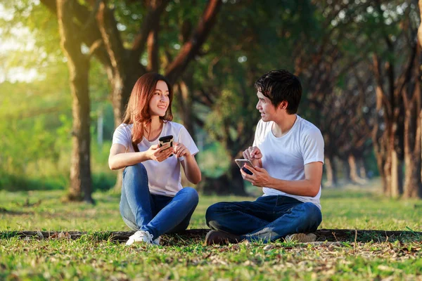 Couple using mobile phone and talking in park — Stock Photo, Image