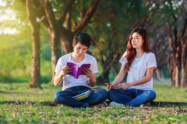 Giovane coppia che legge un libro e ascolta musica con gli auricolari i — Foto Stock
