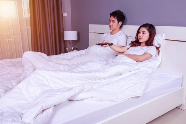 Pasangan muda berbaring di tempat tidur dengan remote control dan menonton tel — Stok Foto