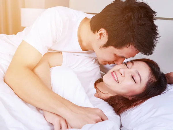 Homem está beijando sua bela esposa sorridente na bochecha na cama — Fotografia de Stock