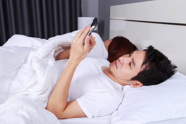Homme utilisant son téléphone portable au lit pendant que sa femme dort nex — Photo