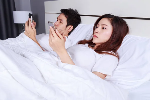 Jeune couple utilisant le téléphone mobile sur le lit dans la chambre — Photo