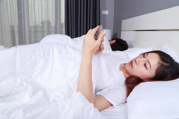 Femme utilisant son téléphone portable au lit pendant que son mari dort — Photo