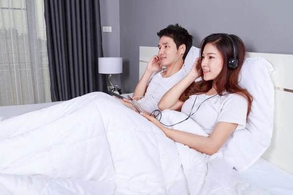 Pasangan mendengarkan musik dari ponsel dengan headphone di tempat tidur — Stok Foto