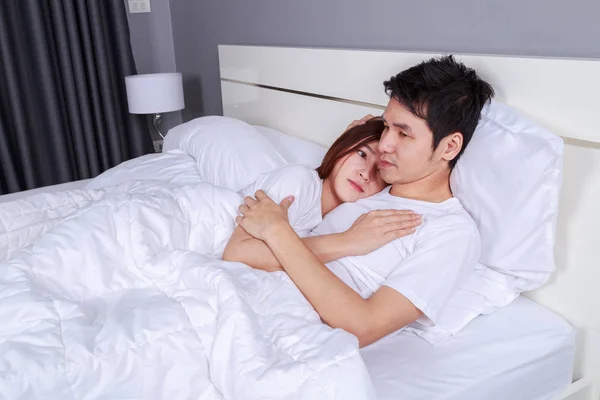 Feliz jovem casal atraente abraçando na cama no quarto — Fotografia de Stock