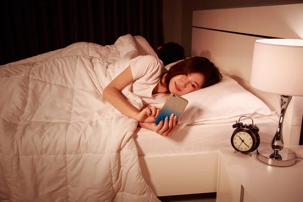 Vrouw met behulp van haar mobiele telefoon in bed's nachts terwijl haar echtgenoot ik — Stockfoto