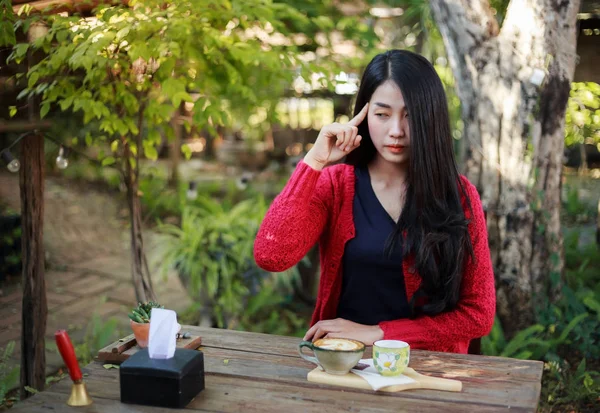 Женщина думает и сидит на столе с кофе в саду — стоковое фото
