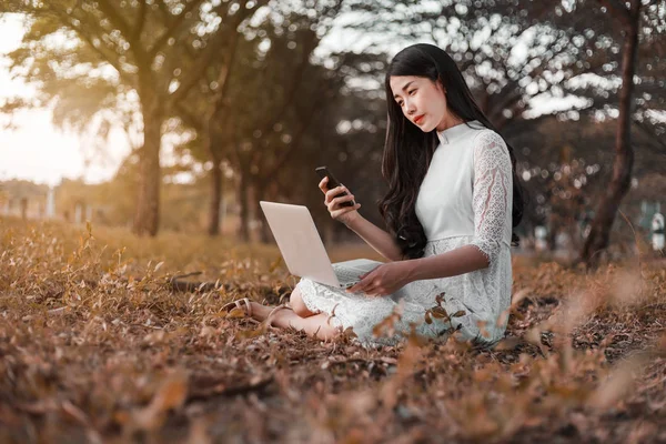 Красивая женщина с помощью ноутбука и мобильного телефона в парке — стоковое фото