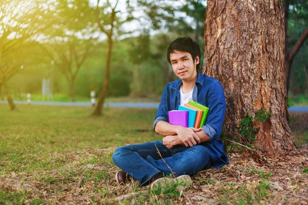 Ung man sitter och håller en bok i parken — Stockfoto