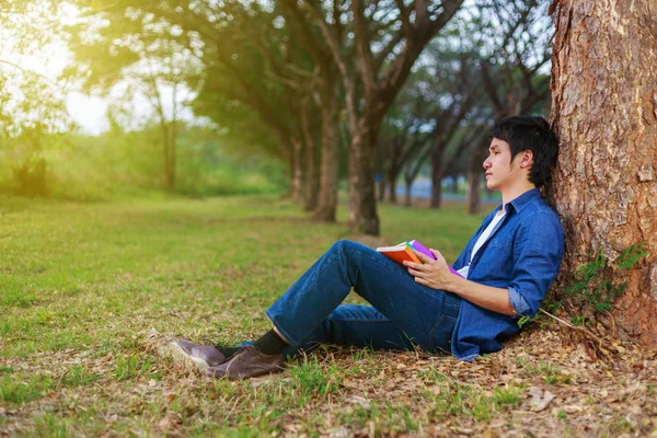 Ung man sitter och håller en bok i parken — Stockfoto