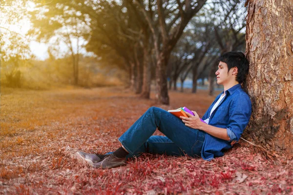 Ung man sitter och håller en bok i parken — Stockfoto