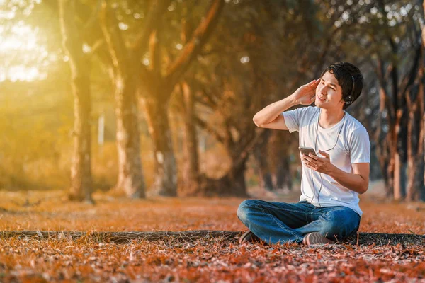 Jeune homme écoutant de la musique avec des écouteurs mobiles dans le parc — Photo