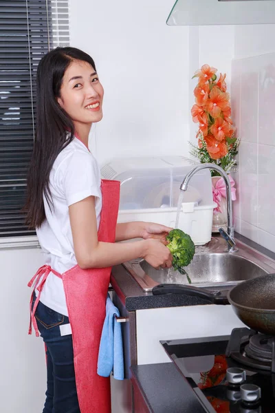Woman washing broccoli under running water at the kitchen sink — Stock Photo, Image