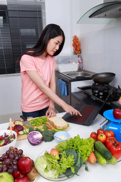 Женщина приготовления пищи и глядя с ноутбуком в кухне комнате — стоковое фото