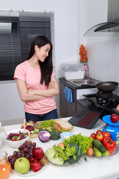 Mulher cozinhar e olhar com laptop na sala de cozinha — Fotografia de Stock