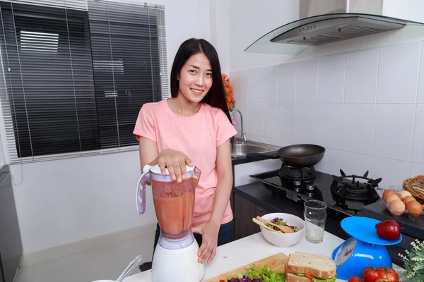 woman making vegetable smoothies with blender in kitchen