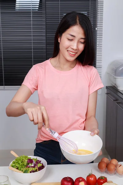 Женщина готовит и взбивает яйца в миске на кухне — стоковое фото