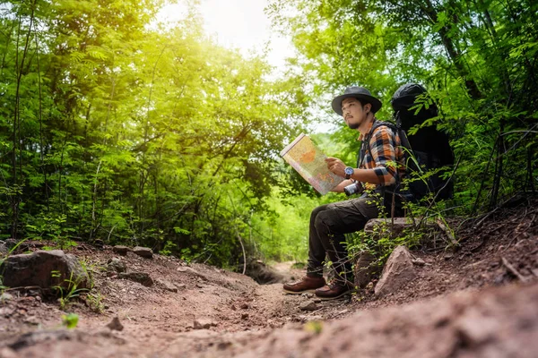 Homme voyageur avec sac à dos assis et la carte de lecture dans la forêt — Photo