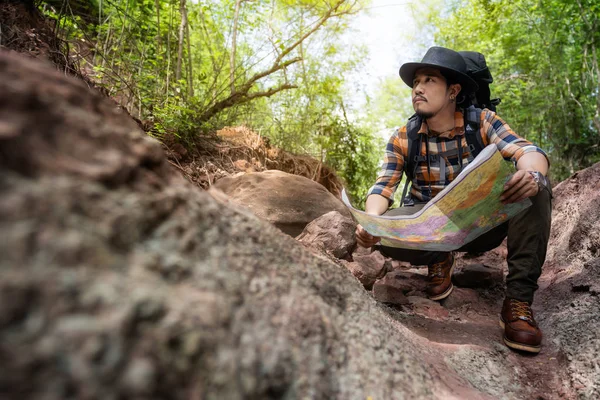 Man traveler with backpack sitting and reading map in the forest — Stock Photo, Image